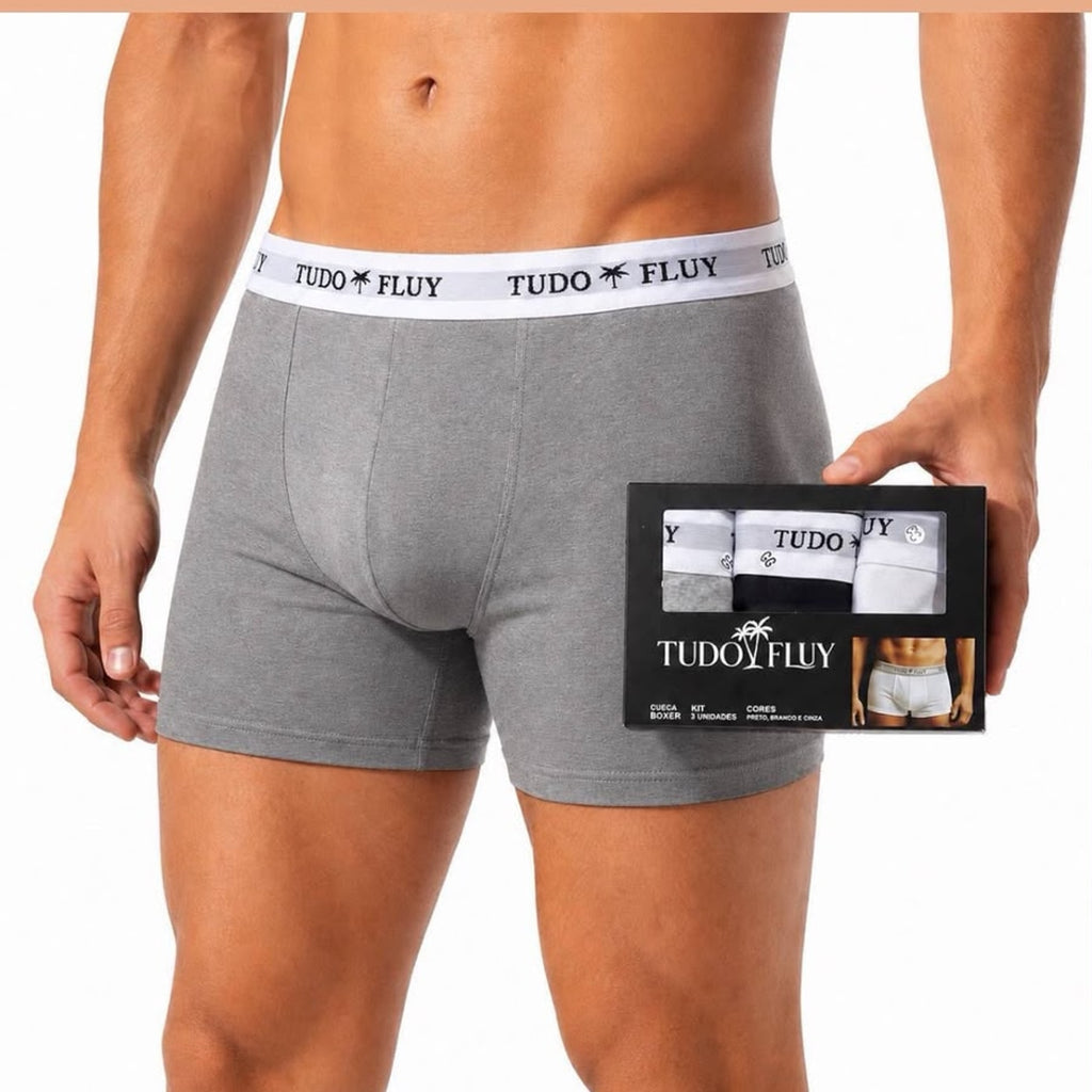 Homem vestindo a cueca boxer Tudo Fluy cinza, segurando a caixa do kit