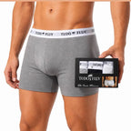 Homem vestindo a cueca boxer Tudo Fluy cinza, segurando a caixa do kit